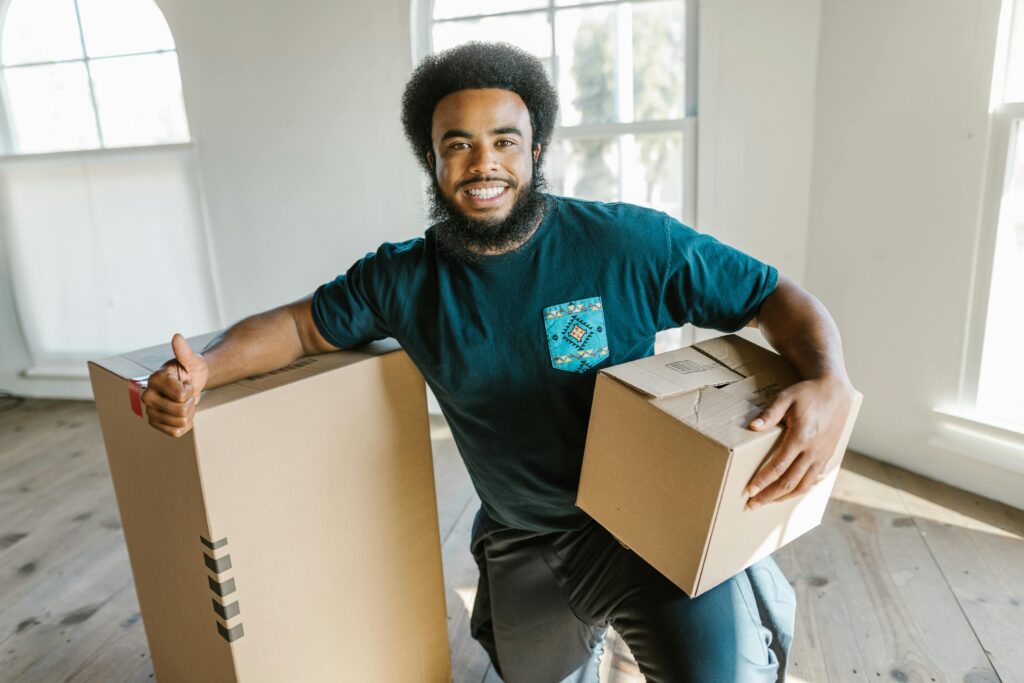 Smiling man with boxes indoors giving thumbs up, perfect for moving-related themes.